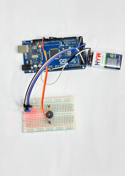Arduino UNO connected to a breadboard using jumper wires, powered by a 9V battery, with mounted IR sensor and buzzer for beginner robotics project.