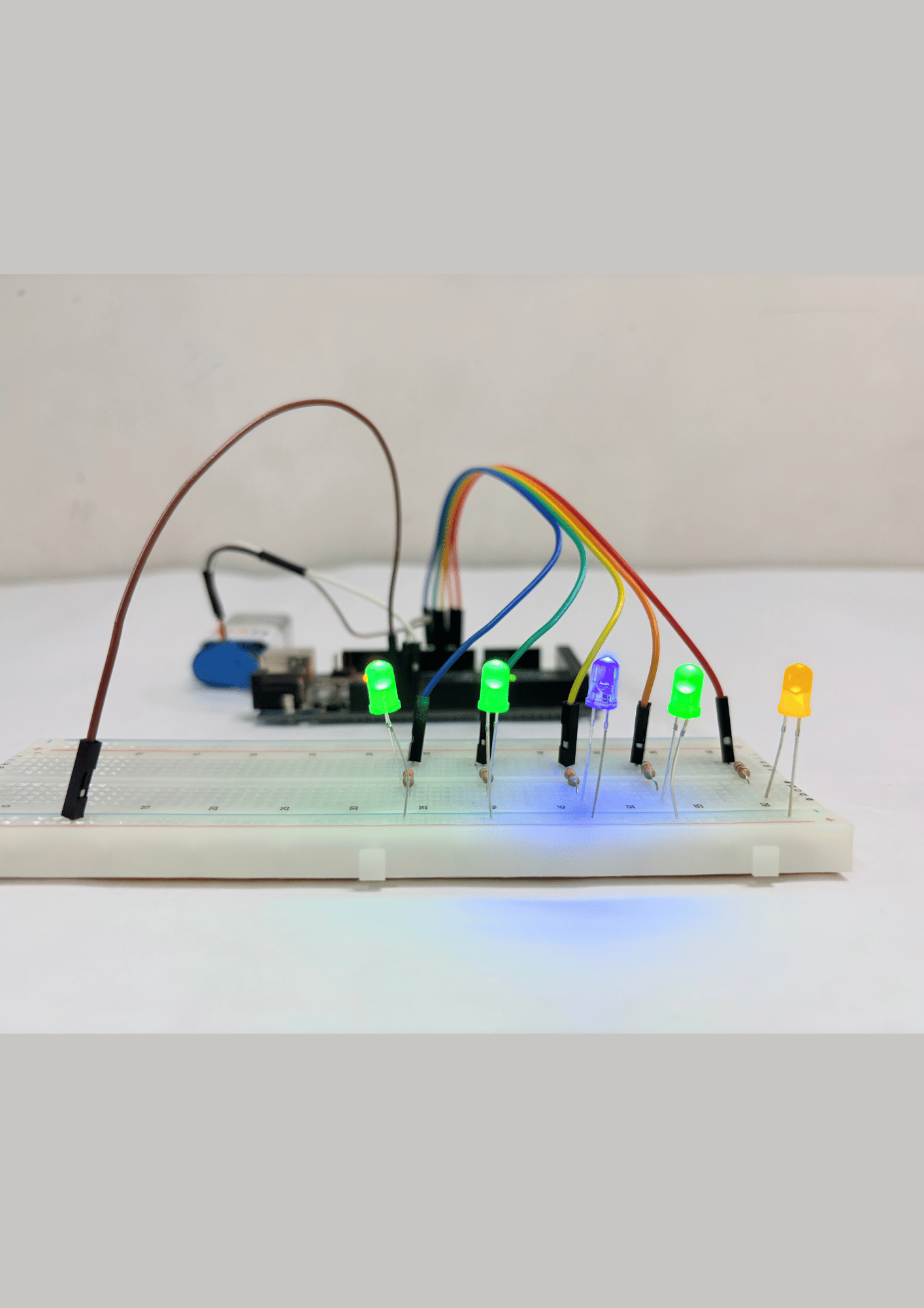 Breadboard with glowing multicolor LEDs connected via jumper wires to an Arduino board for an introductory electronics coding project.