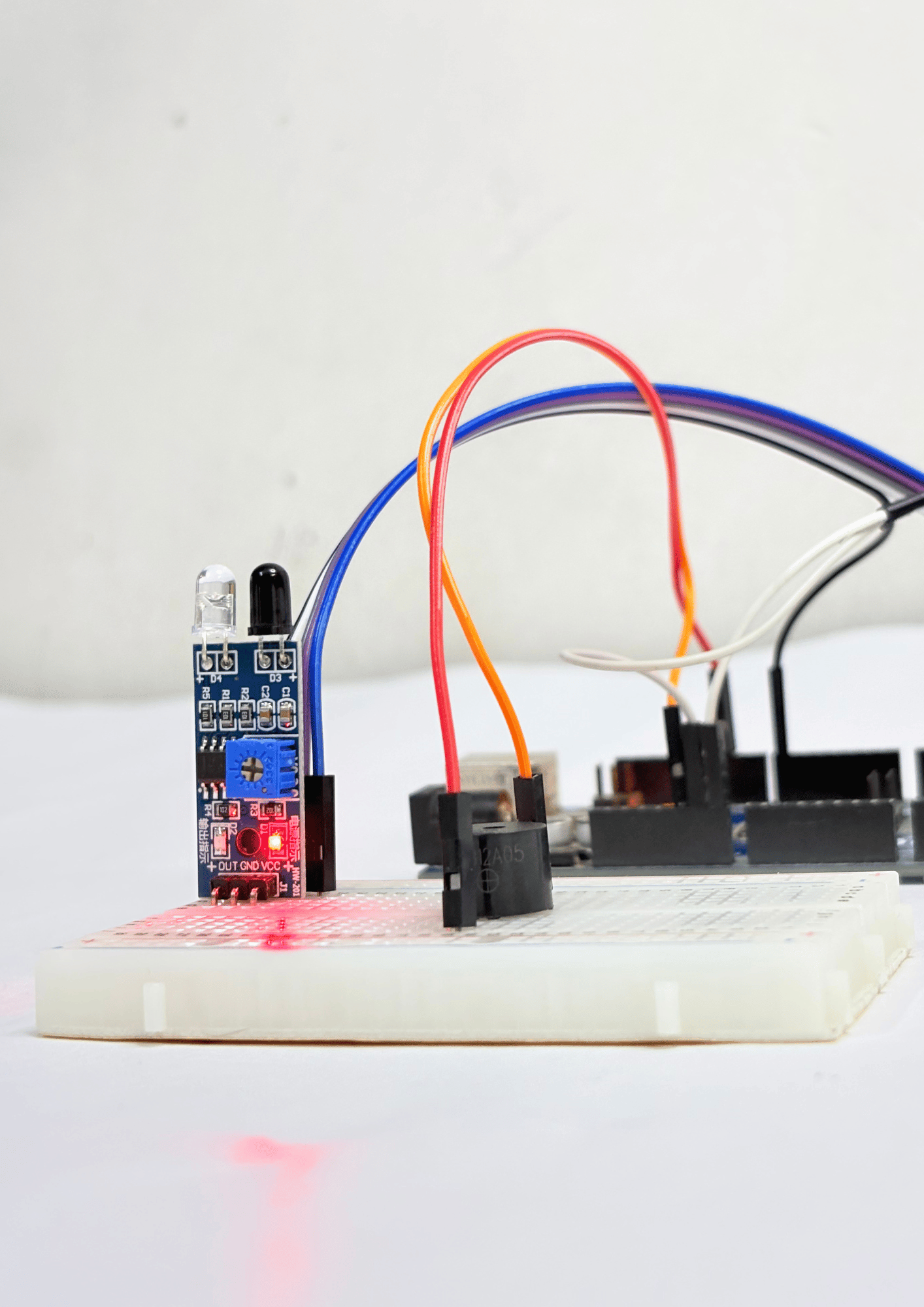 Close-up of an IR sensor module connected to a breadboard with jumper wires, showing red LED indicator while powered and wired to Arduino.
