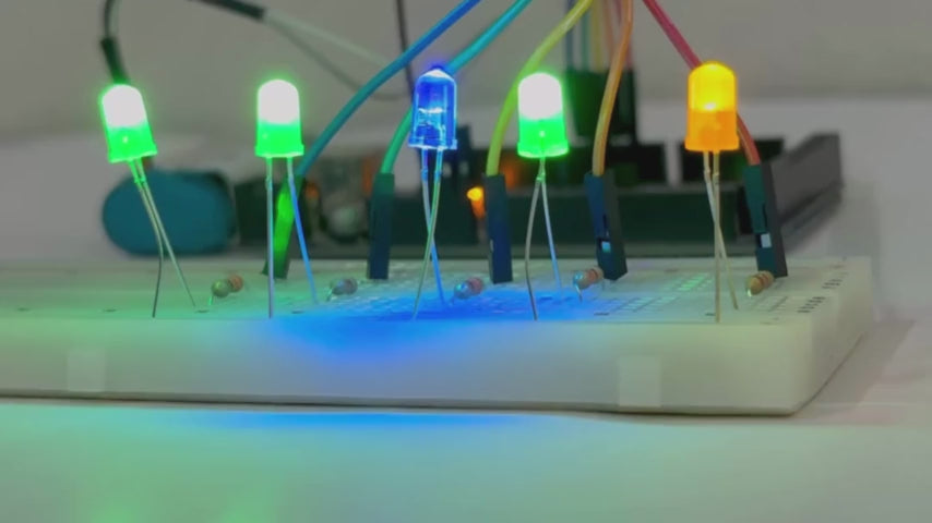 Breadboard with multiple colored LEDs glowing, connected to Arduino with jumper wires for a basic electronics experiment.